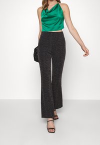 Haut court en satin vert à col halter, associé à un pantalon noir évasé taille haute orné de taches multicolores et  à la texture lisse.