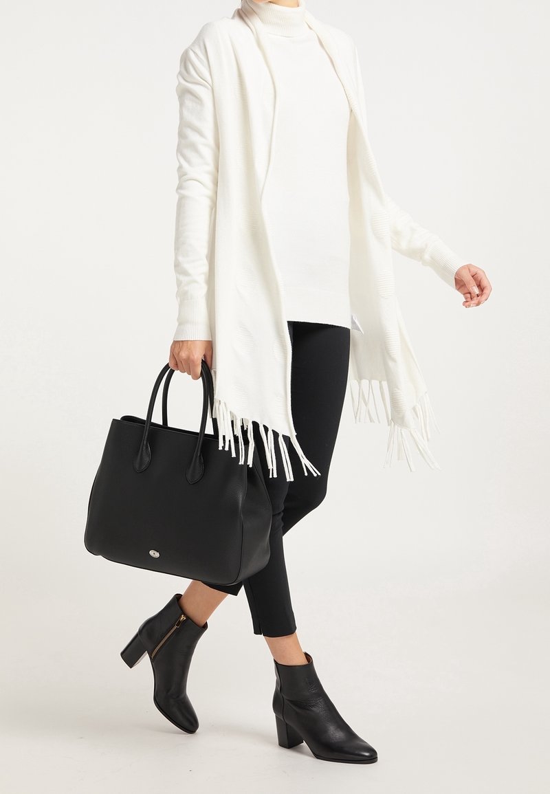 Sac en cuir noir avec deux poignées, surface texturée et accent logo. Associé à un châle blanc, un col roulé et des bottines noires.