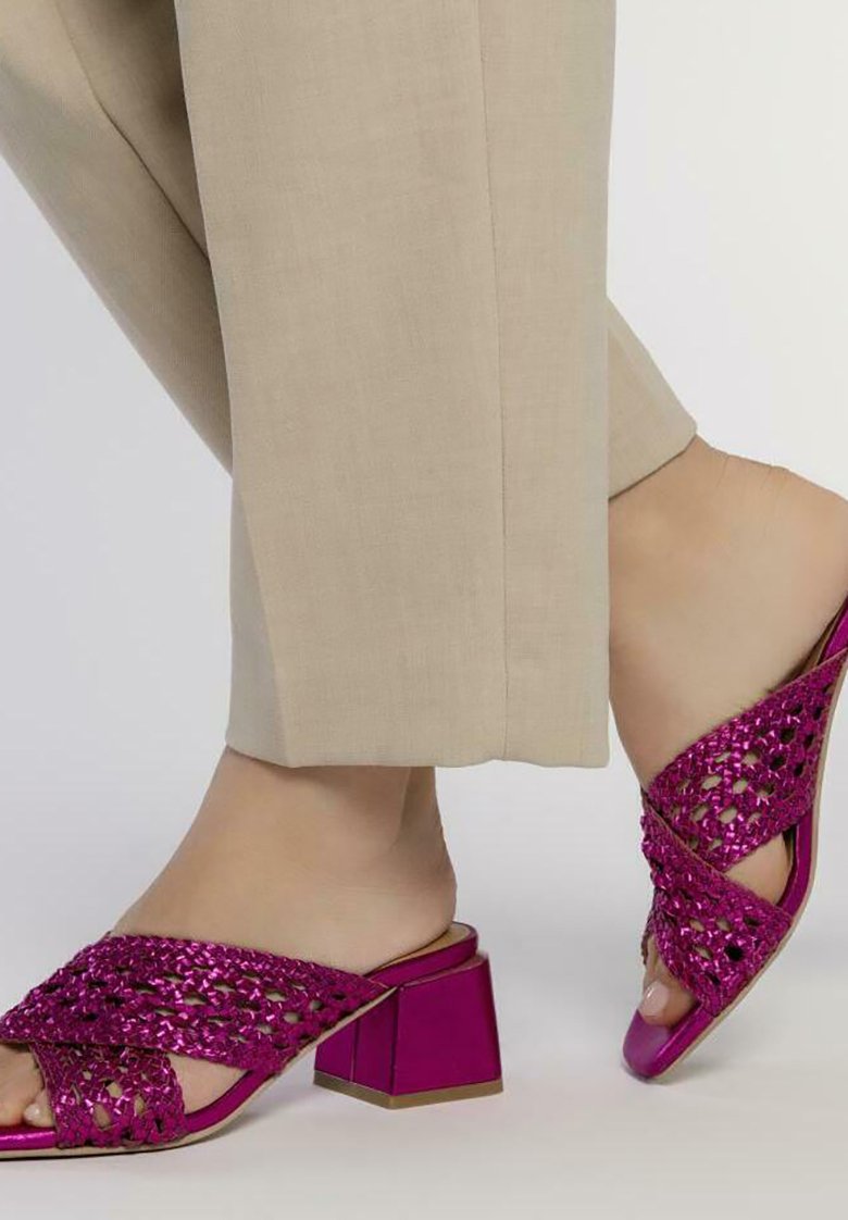 Mules fucsias de tacón con diseño superior trenzado y punta abierta, que presentan un tacón grueso y un acabado metálico brillante.