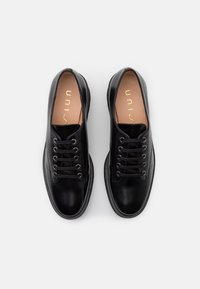 Sneaker nere in pelle con punta rotonda, lacci piatti e occhielli in metallo. Finitura liscia e suole interne imbottite, con un branding minimale all'interno.
