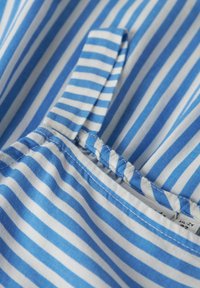 Tissu rayé bleu et blanc avec une texture lisse. Présente des coutures visibles le long du bord et un détail de languette repliée.