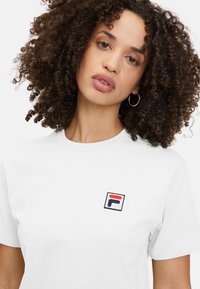 Witte katoenen t-shirt met een klein, geborduurd FILA-logo in blauw, rood en wit op de linker borst. Ronde hals, korte mouwen.