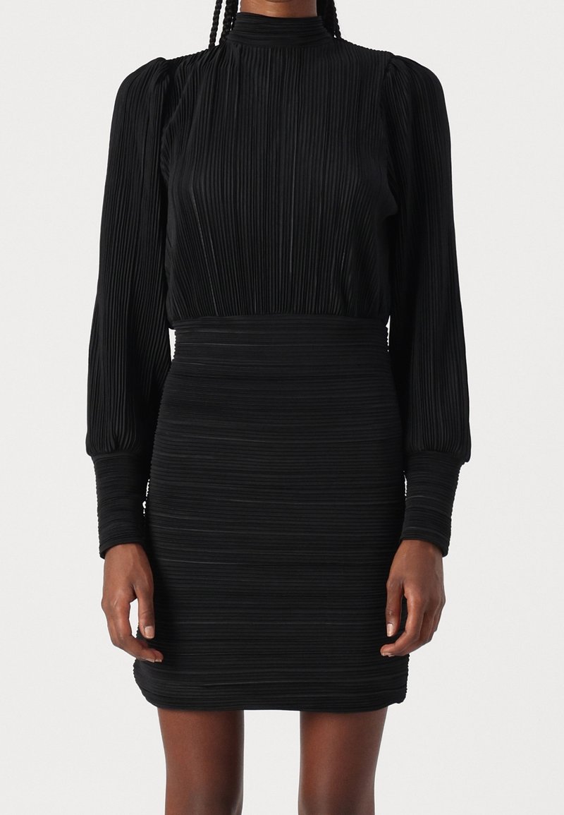 Robe noire plissée avec col montant, manches longues bouffantes et taille cintrée. Tissu texturé avec des rayures horizontales sur toute la surface.