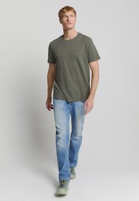 Olijfgroene gestreepte T-shirt met ronde hals, gecombineerd met lichtblauwe jeans en grijze sneakers. Gestructureerde stof met korte mouwen.