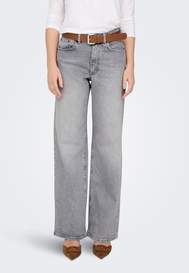 Wide-leg gray jeans with speckled pattern, featuring front pockets and a brown leather belt. Model wears brown heeled shoes.