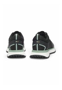 Sneakers nere in mesh con accenti verdi e bianchi, viste da dietro su sfondo bianco.