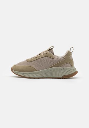 Jasnobrązowy sneaker na sznurowadła z teksturowaną tkaniną na cholewce, uchwytami na języku i pięcie oraz grubą wzorzystą podeszwą z gumową podeszwą zewnętrzną.