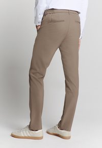Beige broek met een taps toelopende pasvorm, elastische tailleband en twee achterzakken, gecombineerd met witte sneakers met beige accenten.