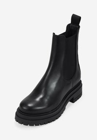 Botín negro de cuero hasta el tobillo con paneles laterales elásticos y una lengüeta de tiro. Presenta una suela de goma gruesa con un dibujo texturizado para mayor agarre.