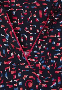 Tissu à motifs avec un mélange de formes géométriques et de lettres rouges, bleues et blanches sur un fond bleu marine foncé, avec un design à col en V.