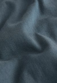 Közelkép egy texturált kék szöveten, amelyen látható a szövés mintázata, és puha redők keletkeznek, amelyek lágy árnyékokat és kiemeléseket hoznak létre.