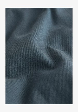 Nahaufnahme eines strukturierten blauen Stoffes mit sichtbarem Webmuster und sanften Falten, die sanfte Schatten und Lichtspiele erzeugen.