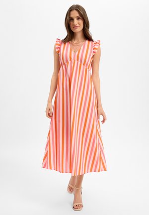 Woman wearing a sleeveless V-neck dress with pink and orange vertical stripes and ruffled shoulder details, standing in neutral sandals.