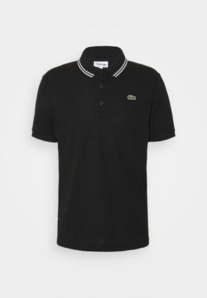 Polo noir à manches courtes avec trois boutons, double bandes blanches sur le col et petit logo crocodile vert brodé sur la poitrine.