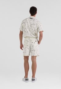 Kurzarmhemd und Shorts-Set mit einem cremigen Grundton und abstrakten Schwarz- und Blaumustern, aus leichtem Stoff gefertigt, mit einem elastischen Bund.