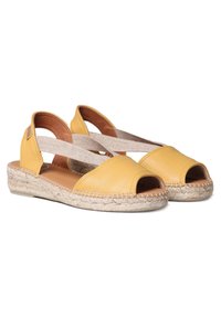 Sandali espadrilles in pelle gialla presentano una punta aperta, fasce incrociate elastiche e una suola a cuneo avvolta in iuta. Texture liscia.