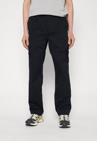 Sorte cargo bukser lavet af letvægtsmateriale, med en afslappet pasform og flere lommer, parret med gule og sorte sneakers.