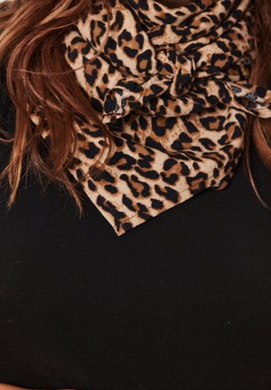Long red hair over black top with leopard print scarf tied in a knot around the neck.