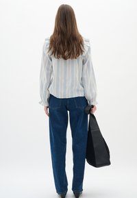 Blusa azzurro chiaro a righe bianche con dettagli arricciati, abbinata a jeans a vita alta blu scuro. Una borsa nera è tenuta nella mano destra.