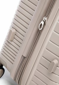 Hard-shell beige suitcase with horizontal ridges, silver zipper partially open, two protective feet, and visible black wheel.