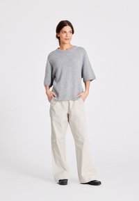 Hallitus halli kootud sviiter, lai kaelus ja lühikesed varrukad, kombinatsioonis kreemikas, lõdva lõikega pükste ja mustade kingadega.