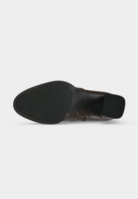 Semelle en caoutchouc noir d'une chaussure en cuir marron à bout pointu, avec une accroche texturée et un talon bloc sur fond blanc.