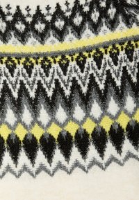 Stickad tröja med ett geometriskt mönster i svart, grått, vitt och gult, med en mjuk yta och livliga accentlinjer.