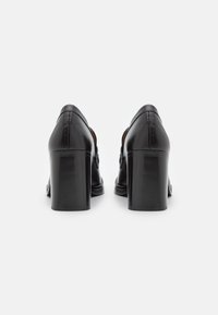 Black high-heeled shoes in smooth leather, featuring a rounded back and a thick, glossy heel. Simple design with minimal accents.