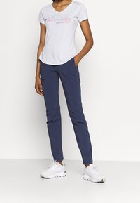 Bílá košile s krátkým rukávem a véčkovým výstřihem, s růžovým logem, spárovaná s tmavě modrými slim-fit kalhotami a bílými sportovními botami. Jednoduchý design, lehká tkanina.