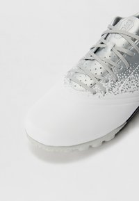 White soccer shoe with a smooth synthetic upper, metallic silver accents, perforated design, and a patterned sole for traction.