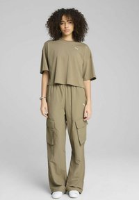 Olivno zeleni skrajšani majica s tiskom, v kombinaciji z ohlapnimi cargo hlačami z stranskimi žepi. Gladka tekstura, sproščen kroj, v kombinaciji z belimi čevlji.