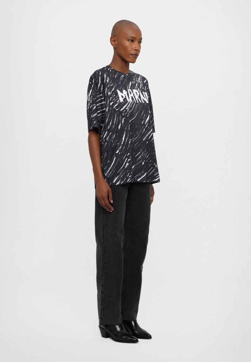 Sort grafisk t-shirt med hvid stribet mønster og fed tekst, parret med mørke grå jeans og sorte hælede ankelstøvler.