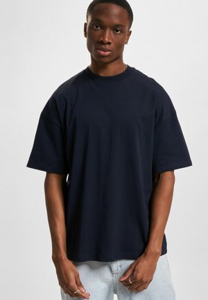 Navy blue cotton t-shirt with a crew neckline and short sleeves, featuring a loose fit and smooth texture, paired with light blue jeans.