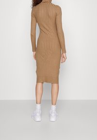 Abito midi a coste in tonalità rame con maniche lunghe e colletto alto, caratterizzato da una silhouette aderente. Abbinato a sneakers bianche e calzini a coste.