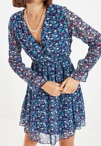 Kukkamekko, jossa on läpinäkyvä tummansininen kangas, pitkät hihat, kietaisuosa ja monivärisiä kukkia vaaleanpunaisena, sinisenä ja vihreänä.