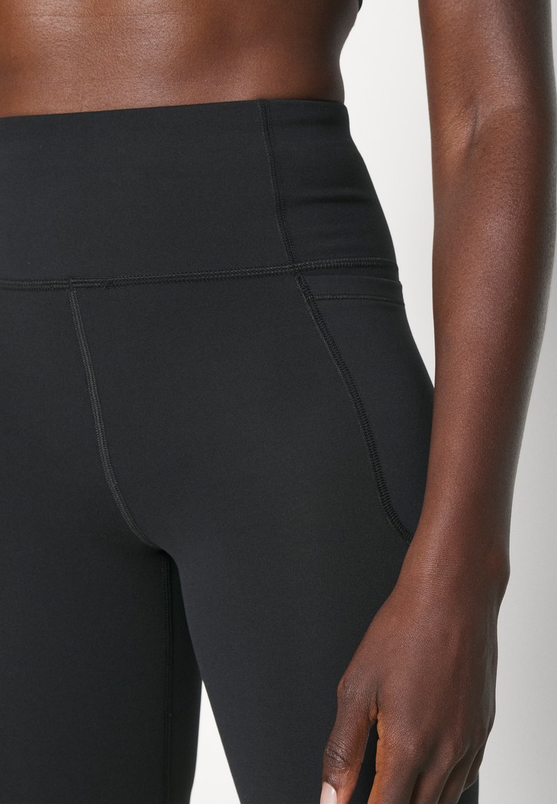 Leggings negros de talle alto con tejido suave y elástico, con costuras planas para mayor comodidad y durabilidad. Vista en primer plano de la cinturilla y la pierna.