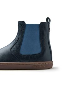 Botín de tobillo azul marino con cuero texturizado, lados elásticos y suela de goma marrón. Presenta una pequeña lengüeta y el logotipo de la marca en el lateral.