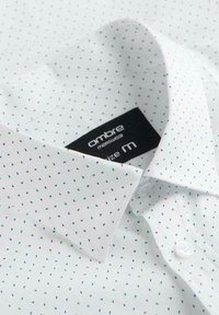 Chemise habillée pour hommes blanche avec motif à petits points bleus et verts, col plié et une étiquette noire indiquant la taille M.