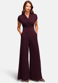 Burgundy jumpsuit with cap sleeves, a wrap neckline, wide-leg design, and side pockets. Made from soft, stretchy fabric.