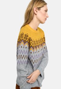 Sweter dziany z żółto-szarym wzorem i geometrycznymi motywami. Bluzka ma okrągły dekolt i długie rękawy.