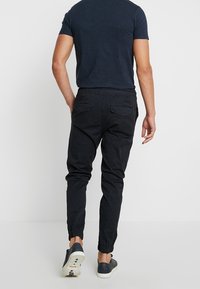 Pantalones de chándal negros con puños elásticos, fabricados en tejido suave. Cuentan con una cinturilla cómoda y bolsillos traseros. Se llevan con zapatos casuales.