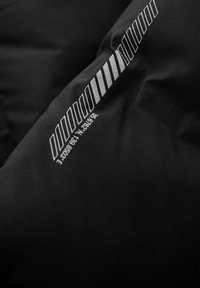 Tejido negro acolchado con una textura suave que presenta franjas gráficas blancas y texto, indicando coordenadas y elevación.