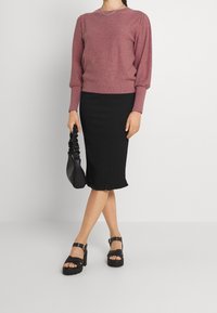 Rosa strukturierter Pullover mit Puffärmeln, kombiniert mit einem schwarzen, gerippten Midirock mit Rüschen Saum, ergänzt durch schwarze Plateau-Sandalen.