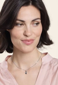 Collana d'argento con un piccolo ciondolo a forma di angelo, impreziosito da dettagli in cristallo. La catena è elegante e arrotondata, perfetta per completare una blusa di un delicato rosa.