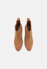 Bottines en cuir suédé marron avec une forme épurée, des panneaux latéraux élastiques et des languettes de traction. Surface texturée avec des coutures visibles.