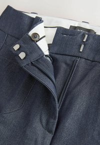 Pantaloni din denim albastru închis cu o textură netedă, având fermoar, închidere cu buton și accente din metal argintiu. Include două buzunare.