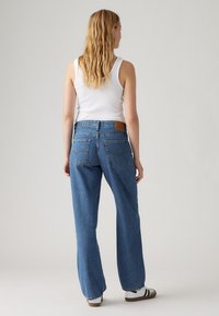 Blauwe denim jeans met een relaxte pasvorm, met een hoge taille, vijf zakken en een bruine leren achterpatch. Het ontwerp heeft een klassieke rechte pijp.