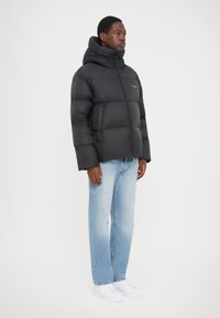 Sort pufferjakke med høj krave, quiltet design og sidelommer. Bæres med lyseblå straight-leg jeans og hvide sneakers.