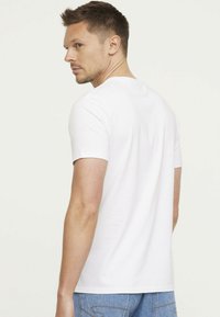 T-shirt blanc à manches courtes en coton, avec un col rond classique et une texture lisse, porté avec un jean en denim bleu.