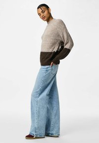 Pull en tricot avec un haut beige clair et un bas marron foncé, associé à un jean en denim bleu à jambes larges. Le pull présente un col rond et des manches longues.
